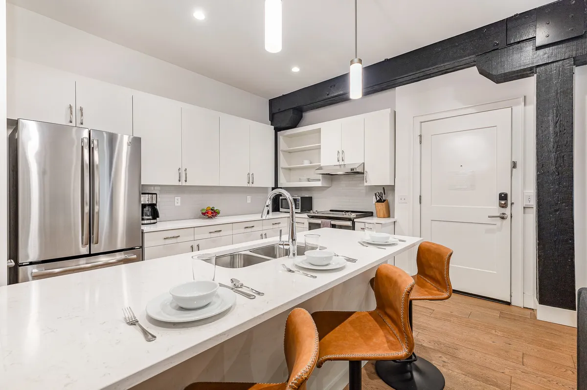 A bright, stylish kitchen with a large island, modern bar stools, stainless steel appliances, and white cabinetry. The setup is perfect for both meal prep and casual dining, with a layout that encourages group interaction.