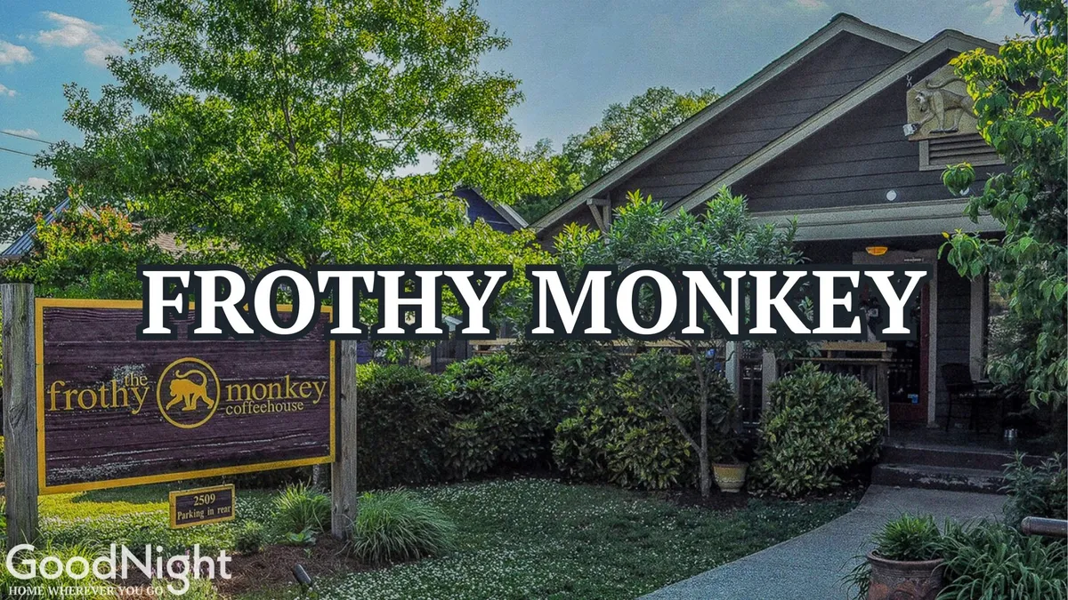 An exterior view of the Frothy Monkey coffeehouse, with prominent signage, a welcoming patio, surrounding greenery, and a glimpse of patrons enjoying the outdoor atmosphere.