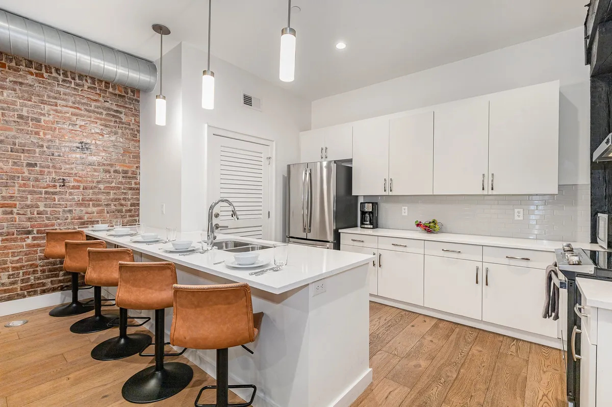 A chic kitchen scene featuring an exposed brick wall, a sleek island bar with stools, and stainless steel appliances. The island serves as a natural hub for casual dining or socializing, with a modern yet cozy vibe.
