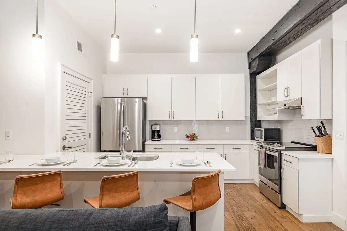 This image showcases a welcoming kitchen centered around a spacious island with bar stools, gleaming stainless steel appliances, and crisp white cabinetry. The countertop is clear and inviting, offering plenty of room for meal prep or communal gatherings.
