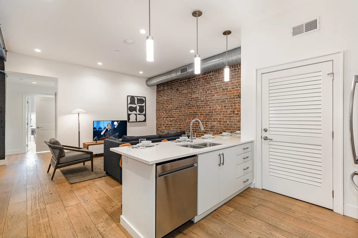 A chic interior view of the loft’s kitchen island, exposed brick wall, and a cozy sofa seating area. The contemporary decor and open-plan layout highlight the modern amenities and social-friendly design, making it a perfect spot for group meals or a casual movie night.